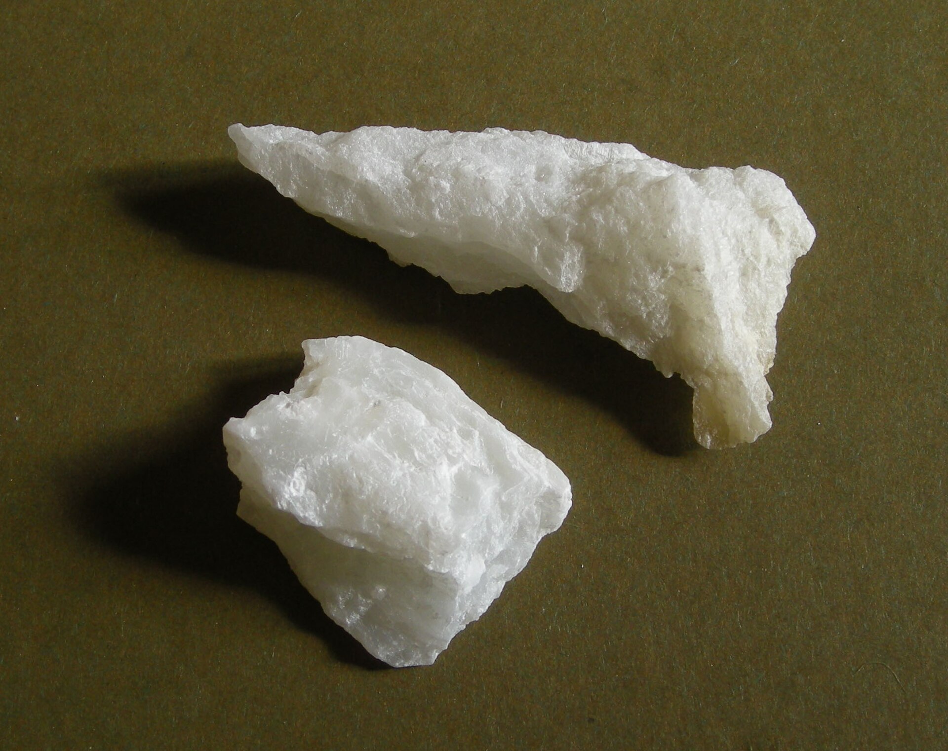 Two white talc lumps on a dark olive background